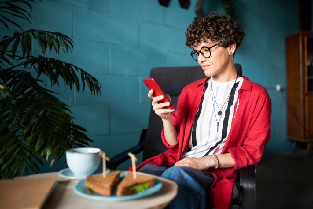 Young brunette female with smartphone surfing in social networks in cafe