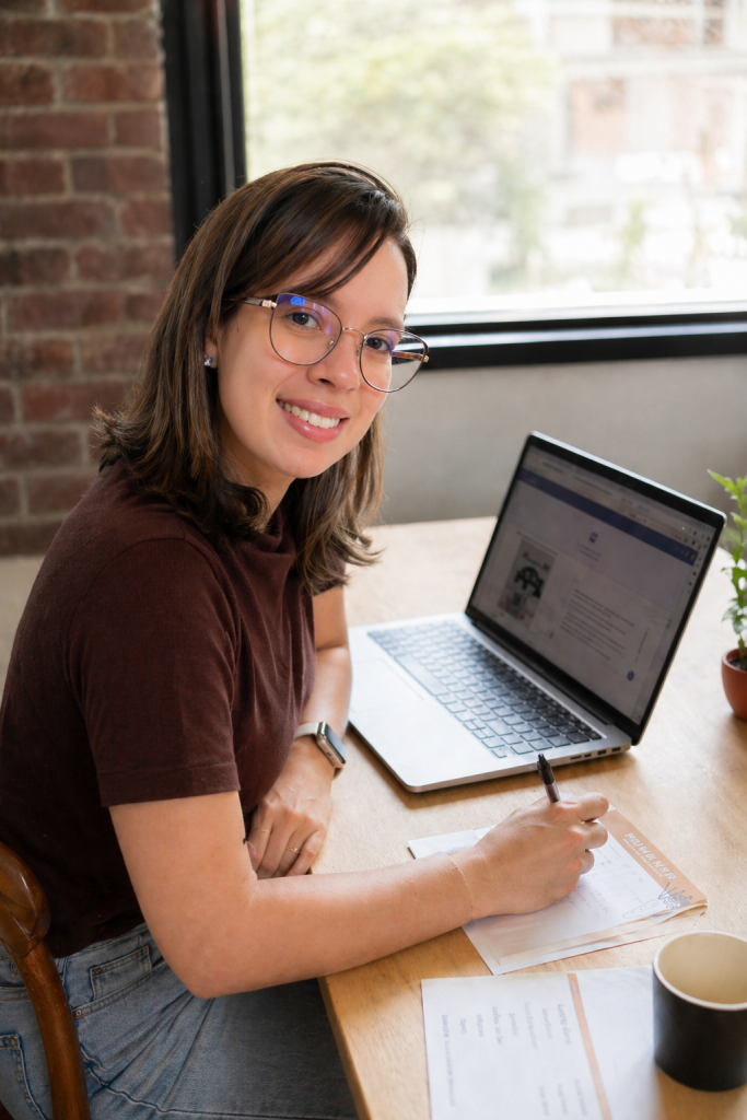 Fernanda Felix sorrindo, escrevendo à mesa com o notebook aberto